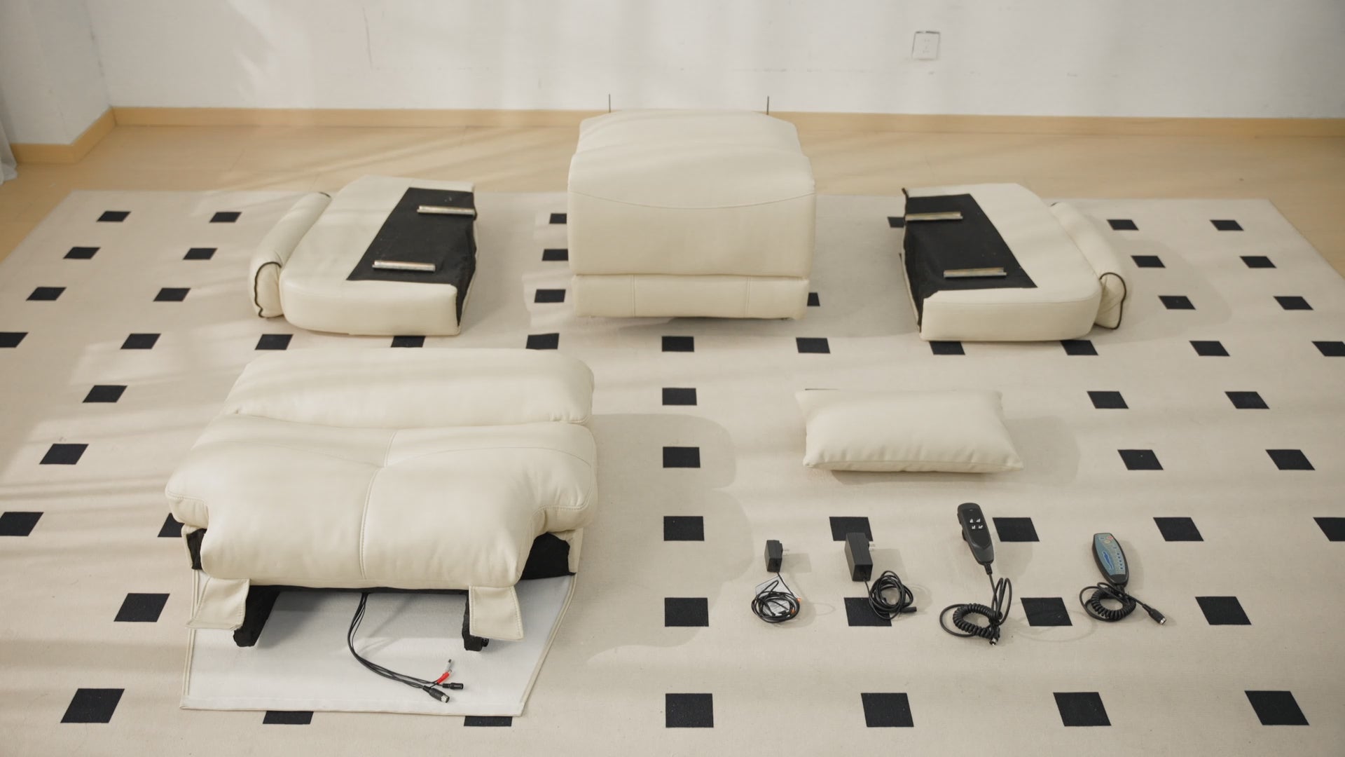 Assembly guide video for cream leather 3-motor power lift recliner, all separate components laid out and labeled: Backrest, Base, Right Armrest, Left Armrest, Head Cushion, and Parts Box containing power adapters & two remote controllers, displayed on checkered floor mat for easy DIY installation instruction.
